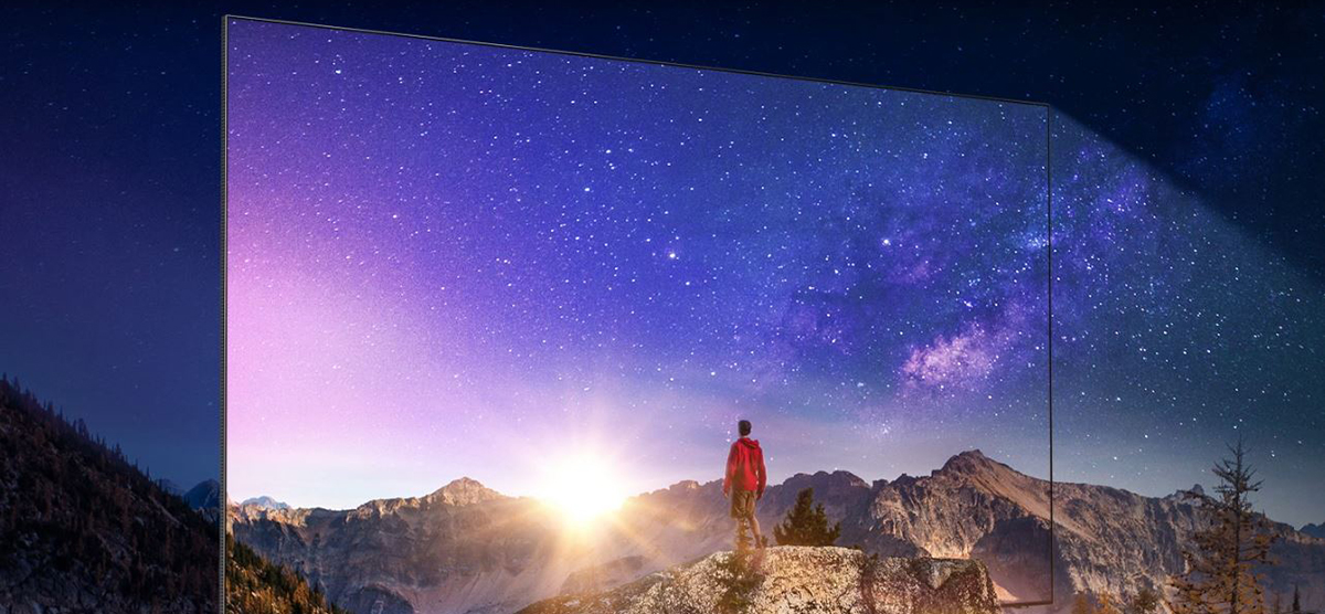 A man is on top of a mountain looking at a magnificent view. QLED's nearly bezel-less frame appears to show the stellar picture and clear contrast.