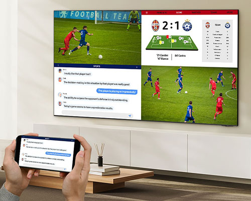 A person watches 4 different screens on their TV simultaneously. They have two screens displaying a soccer match from two different angles, the third screen displaying live stats and the last screen mirroring their mobile as they chat about the game.