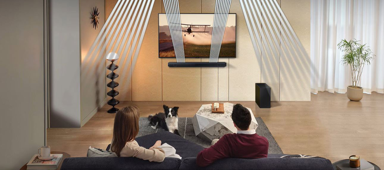 A man and woman are sitting in a living room with sound waves that come out of the Q600C's front and up-firing speakers.