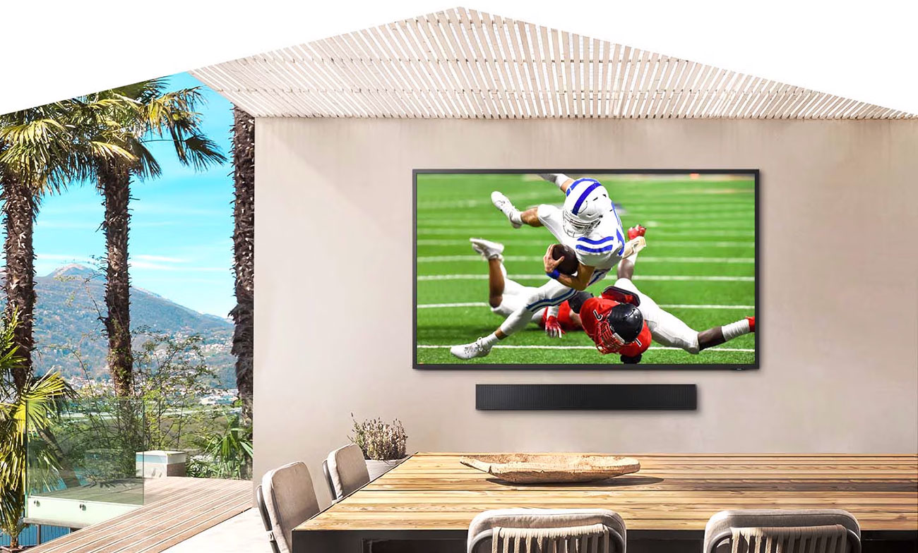 The Terrace is hanging on a white wall outdoors displaying a football match on its screen.