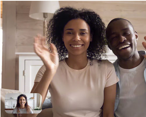 Image of couple in living room waving at a friend during video chat