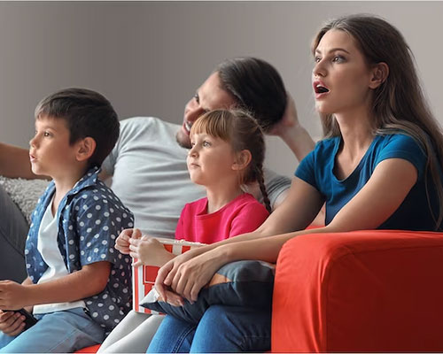 Man and woman with two children on sofa watching TV